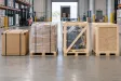 Four commercial freight packaging methods shown side by side: a reinforced carton, palletized cartons, an open wooden frame, and a closed wooden crate.